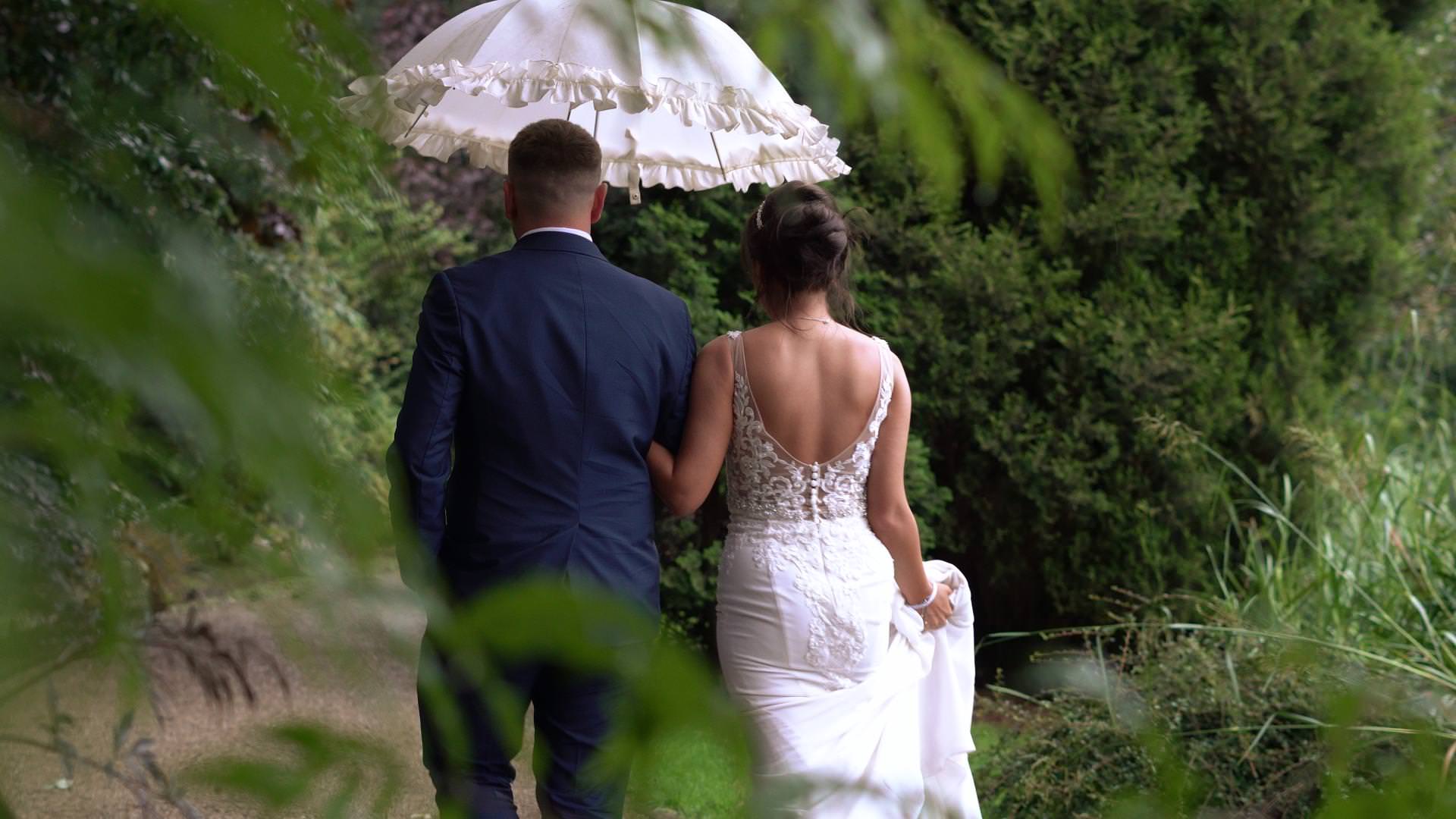a bride and groom walk around the gardens at Moddershall Oaks holding a white umbrella