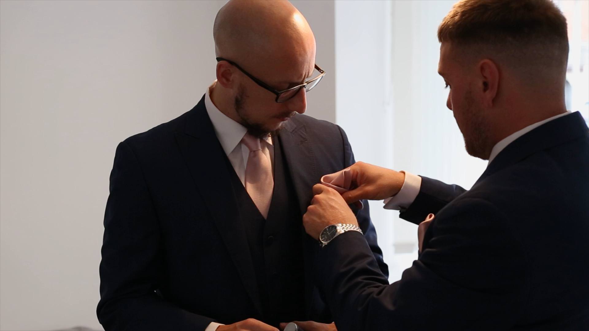 groom putting pink pocket square in to a best mans suit