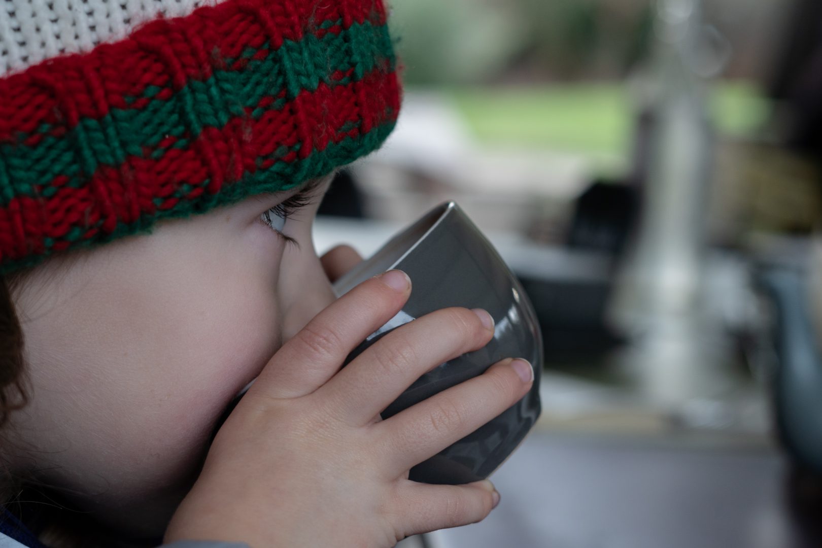 a photograph of a little girl in a wooly hat drinks hot chocolate