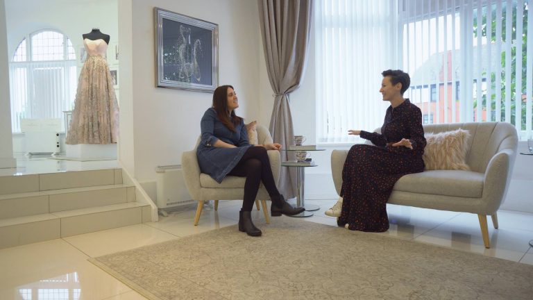 wedding videographer and liverpool bridal boutique owner sit on cream sofas chatting for vlog