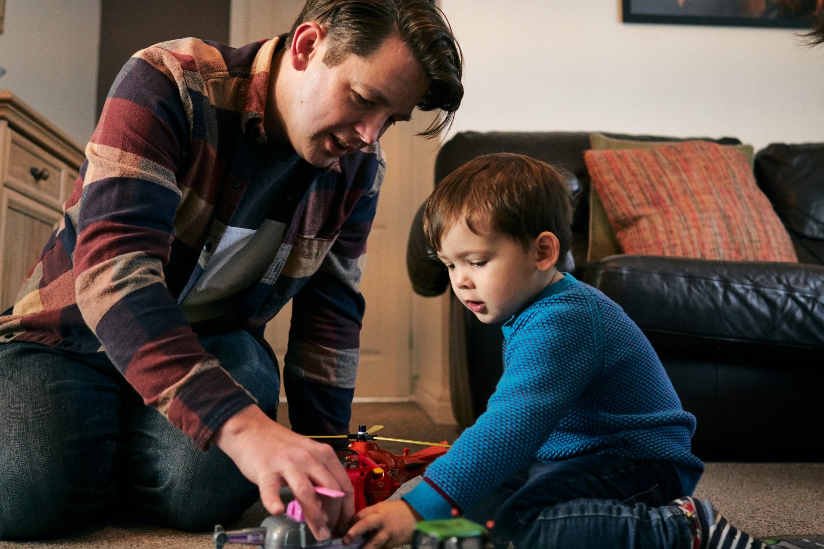 dad and son play with cars on their living room floor