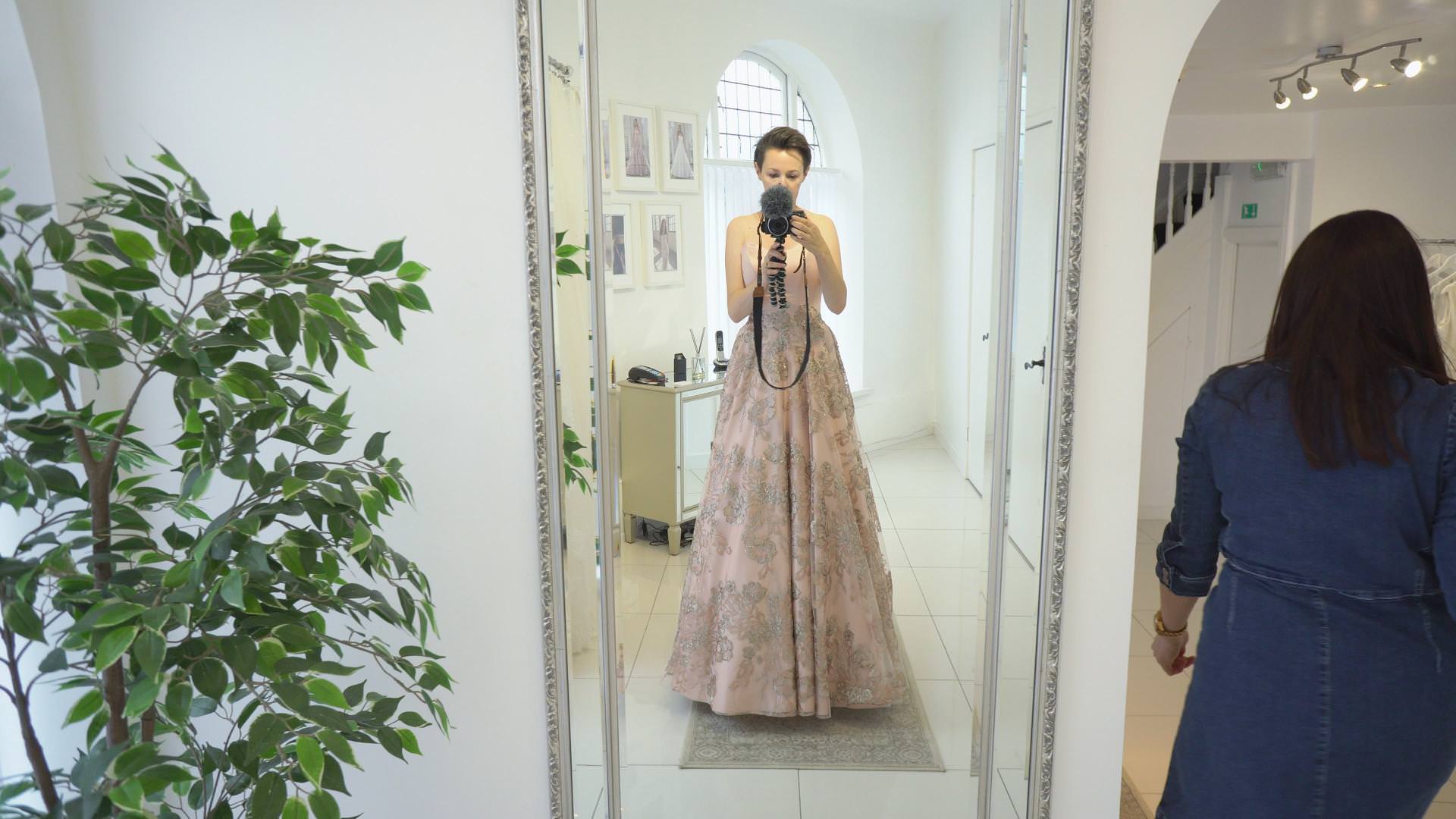 wedding vlogger stands in mirror in a blush pink dress