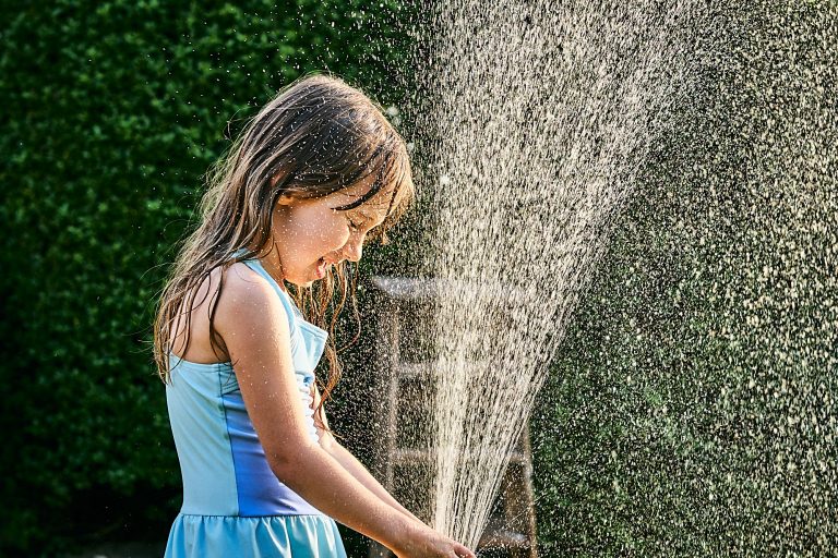 girl plays with hose in garden for photos