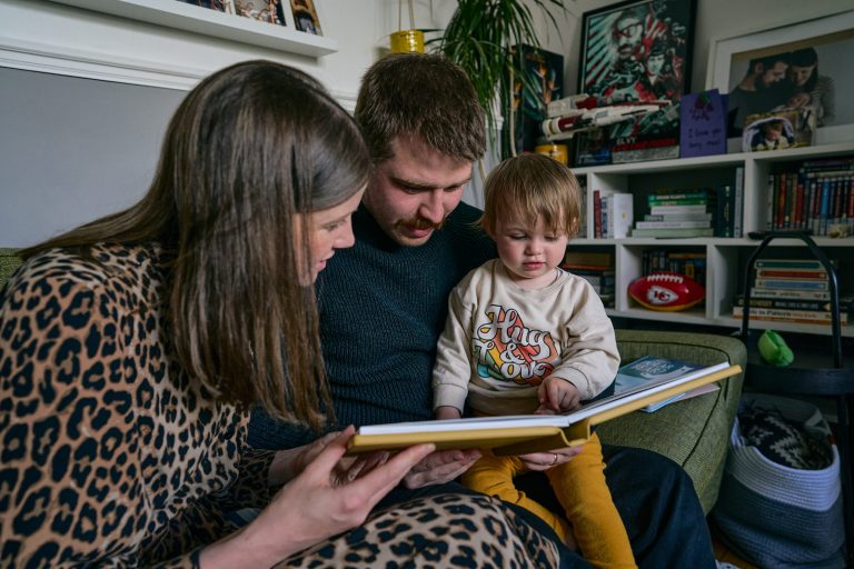 a family sit down together to look over a printed family album at home in Walkden