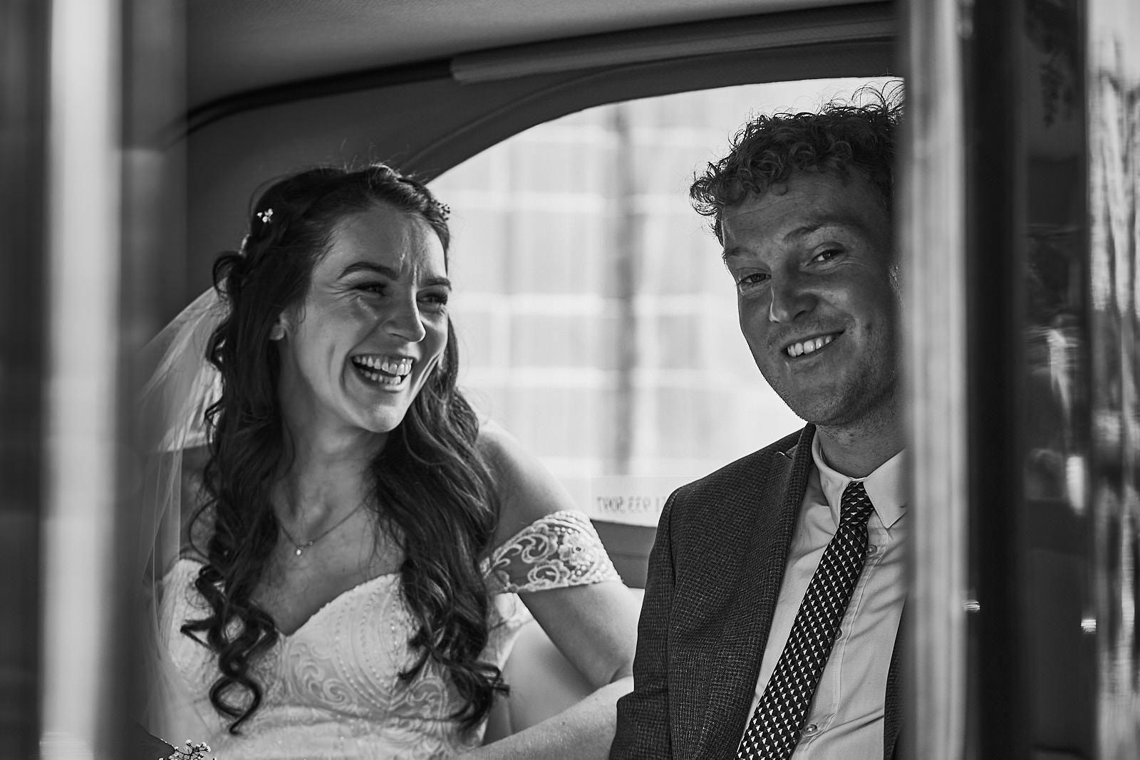bride laughs with groom inside wedding car in liverpool