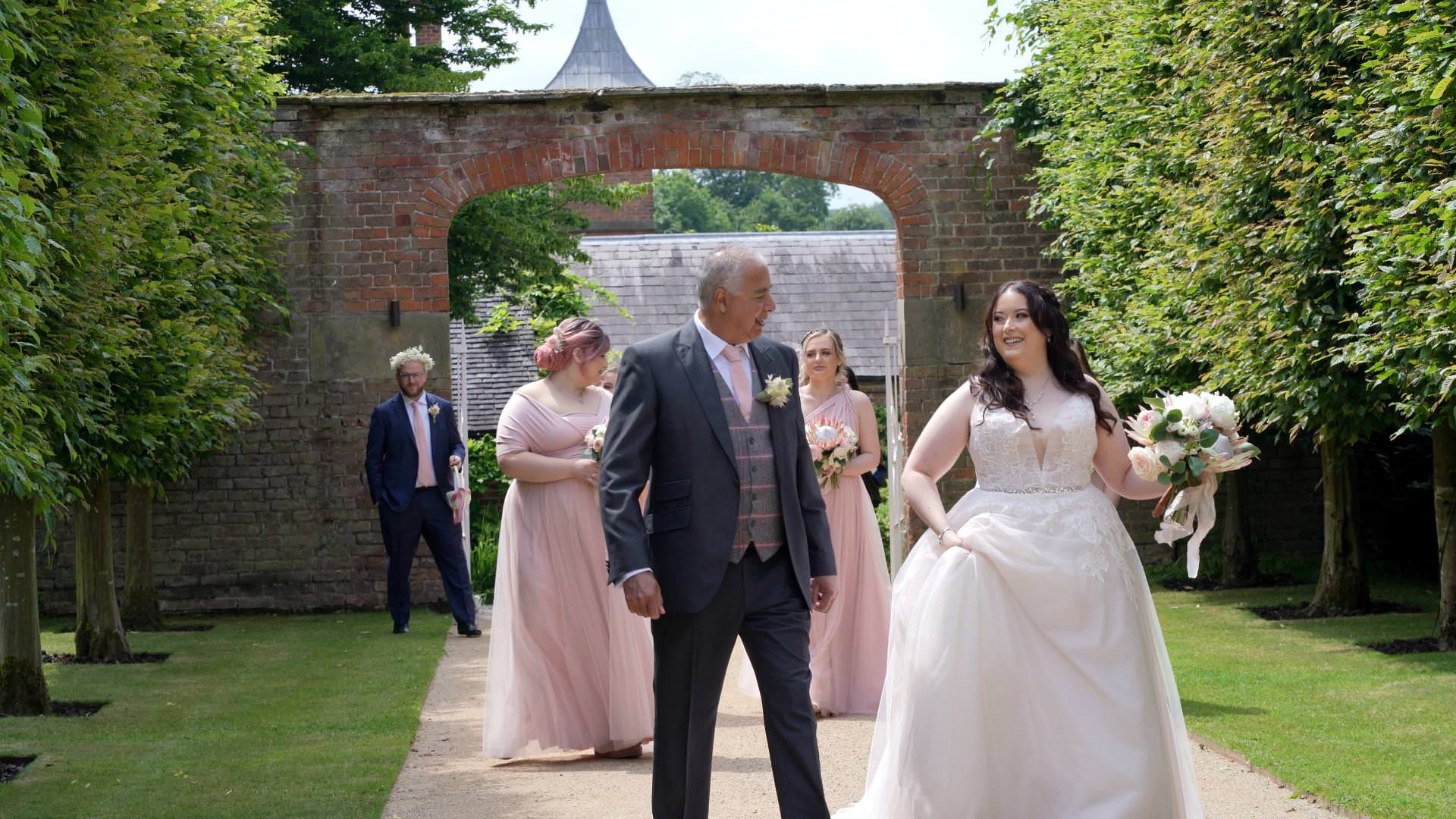 bride walks to outdoor ceremony at Combermere Abbey