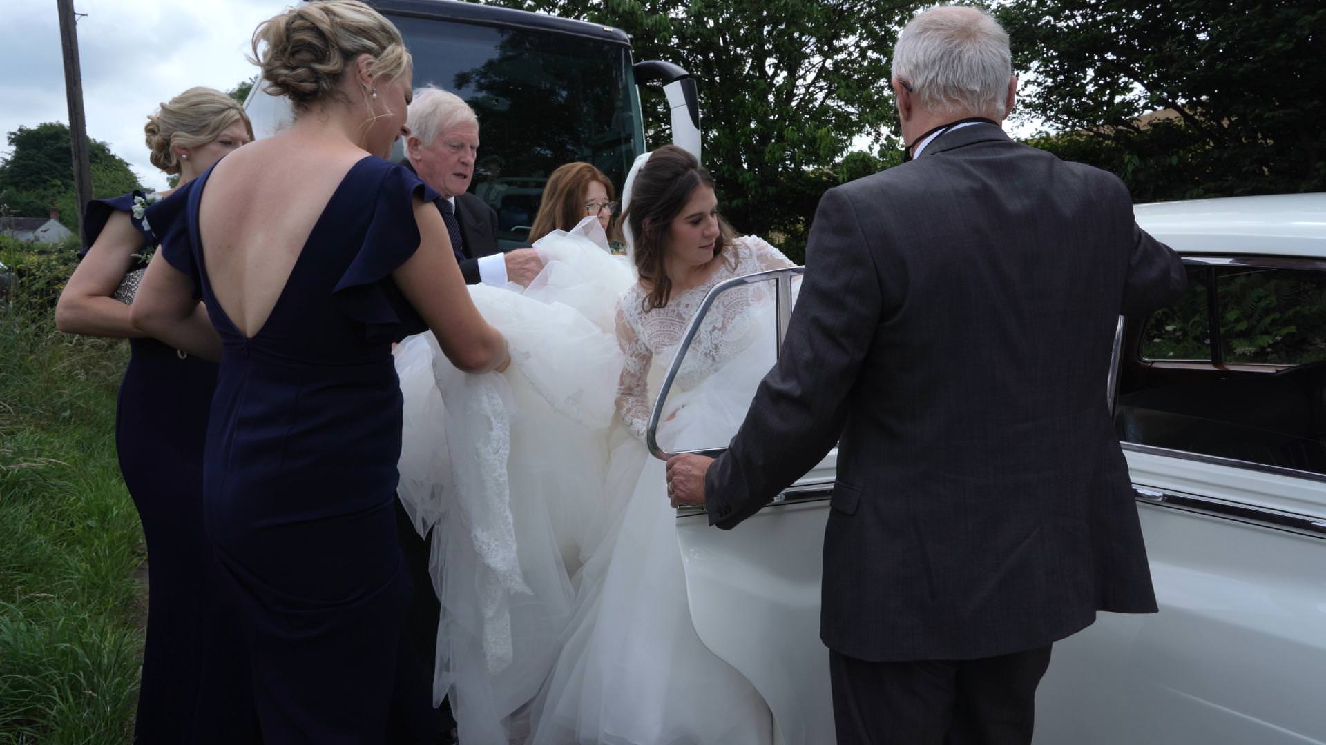 bridal party help bride get big wedding dress in to car