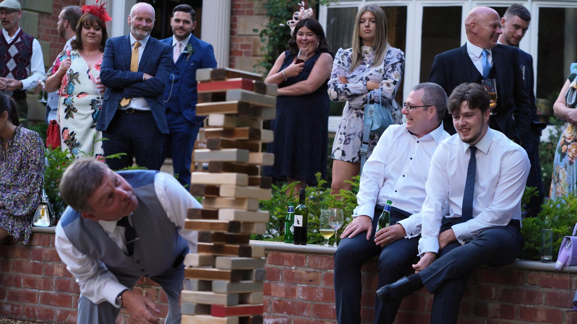 Rebecca and Nathan Ashfield House Wedding 23 wedding guests crowd around Crazy 9 giant jenga game