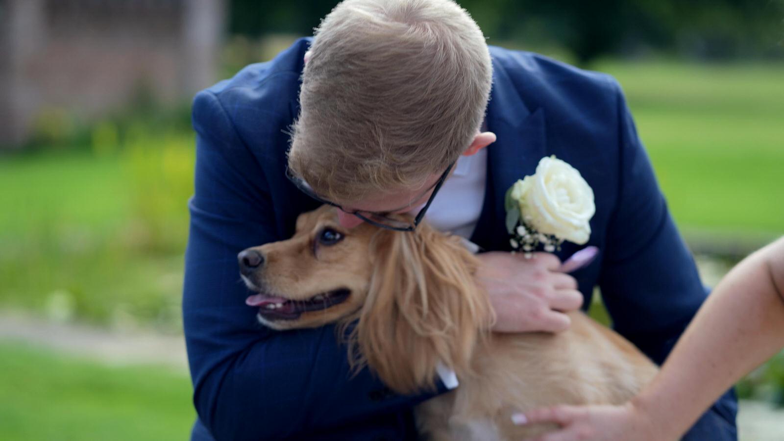 groom cuddles and kisses dog at wedding