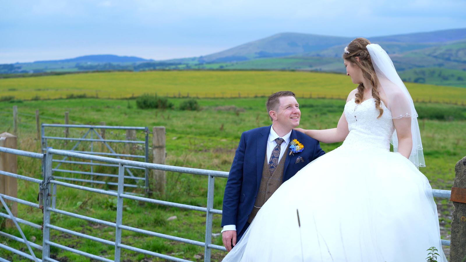 farmer bride and groom sit on fence for video and photos