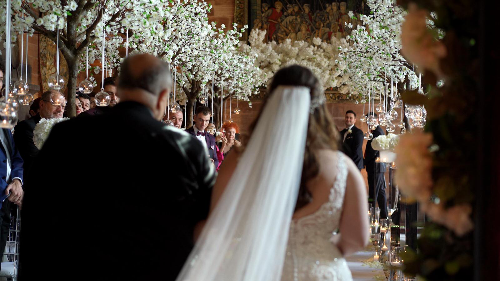 bride walks down white blossom aisle at peckforton castle