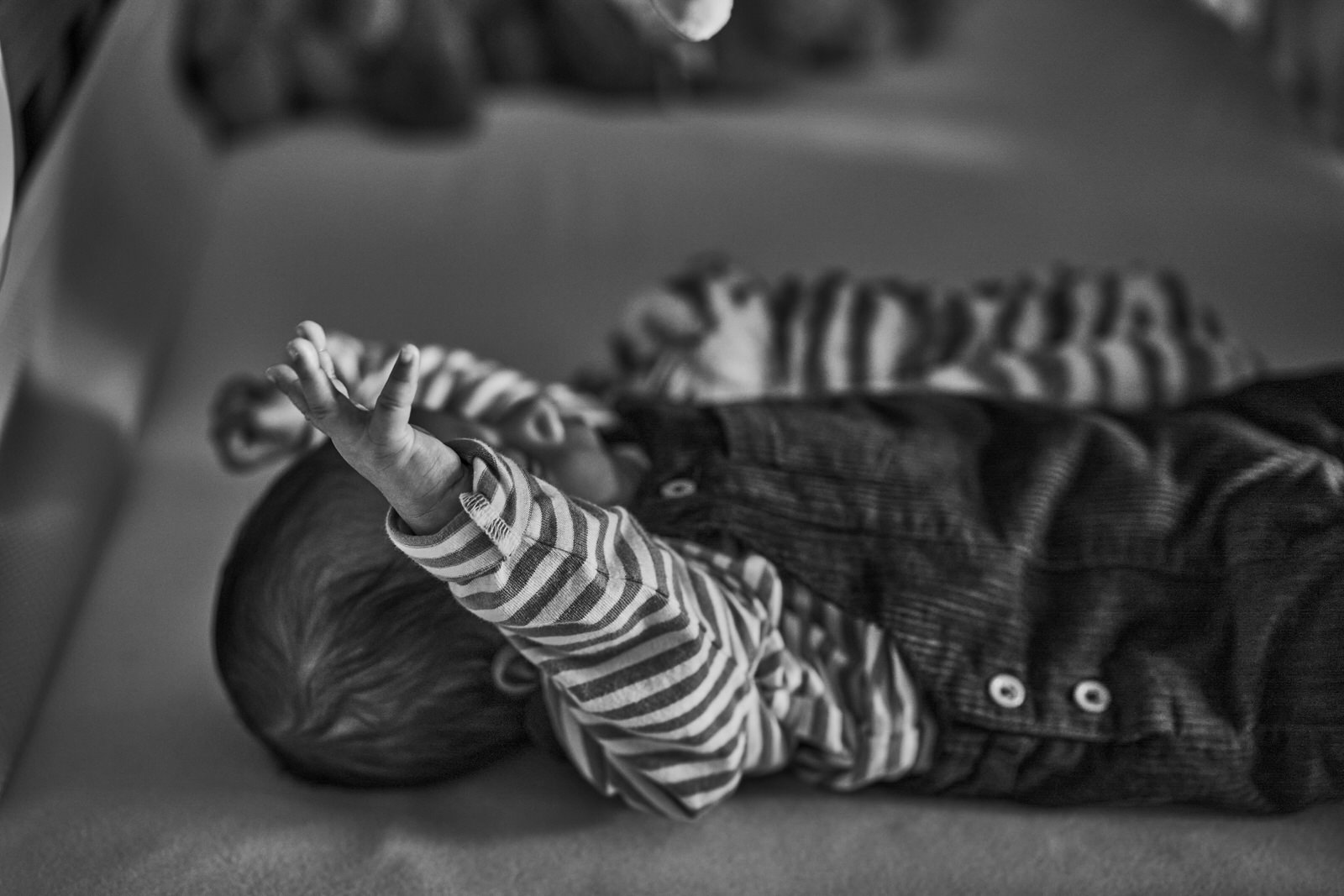 black and white photo of baby stretching in cot