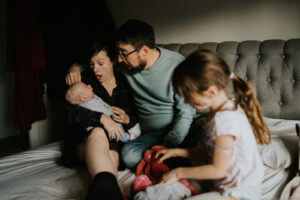 family sit on bed during photoshoot with baby