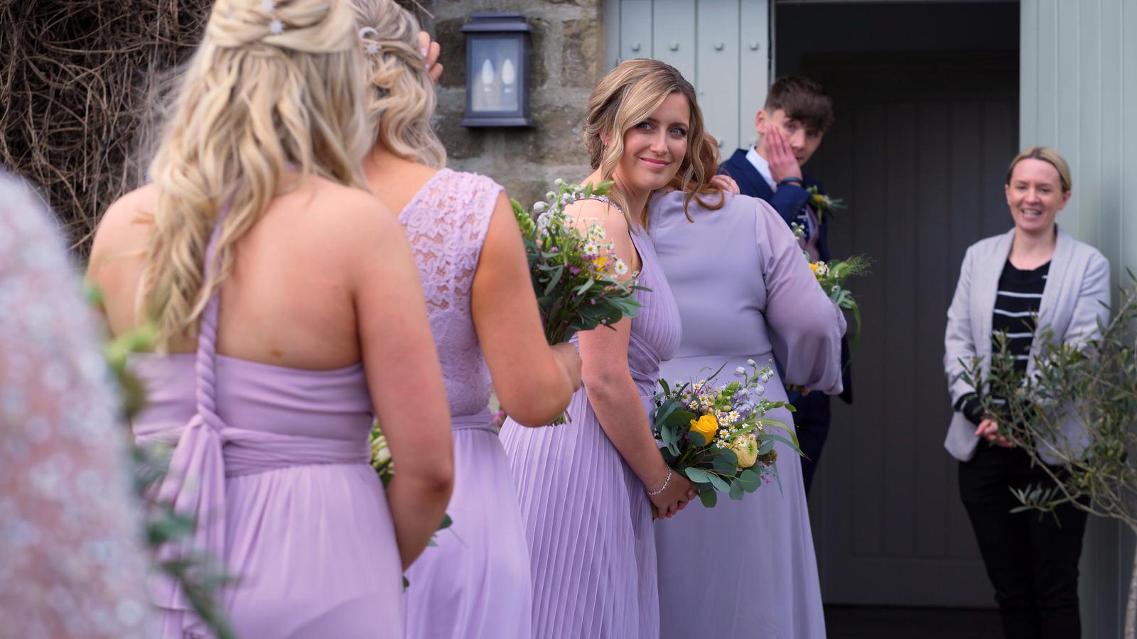 bridesmaids smile and wait outside barn ceremony