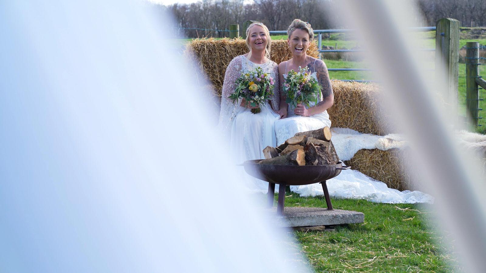 two brides laugh on a hay bale outside Chilli Barn Otley