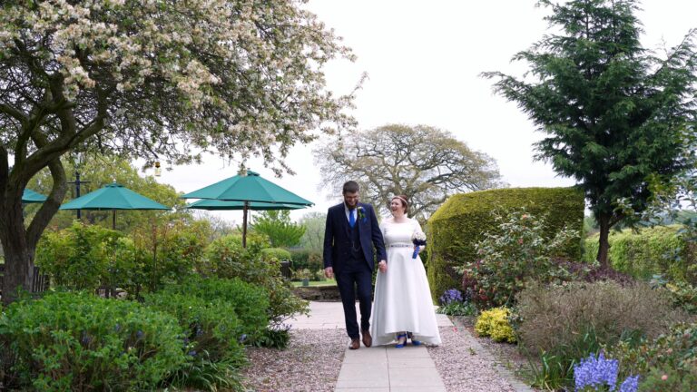 couple smile and walk for videographer outside Rookery Hall