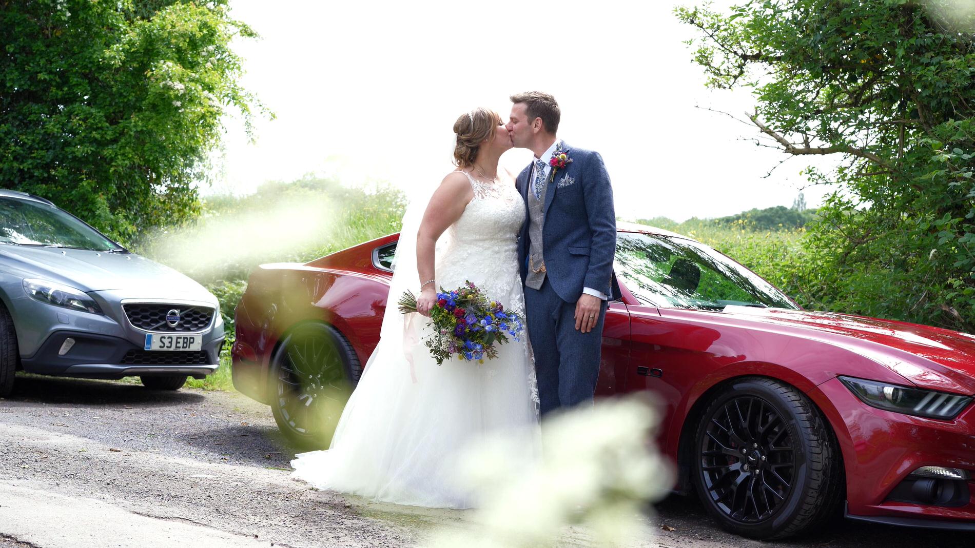 couple kiss next to their Mustang wedding car