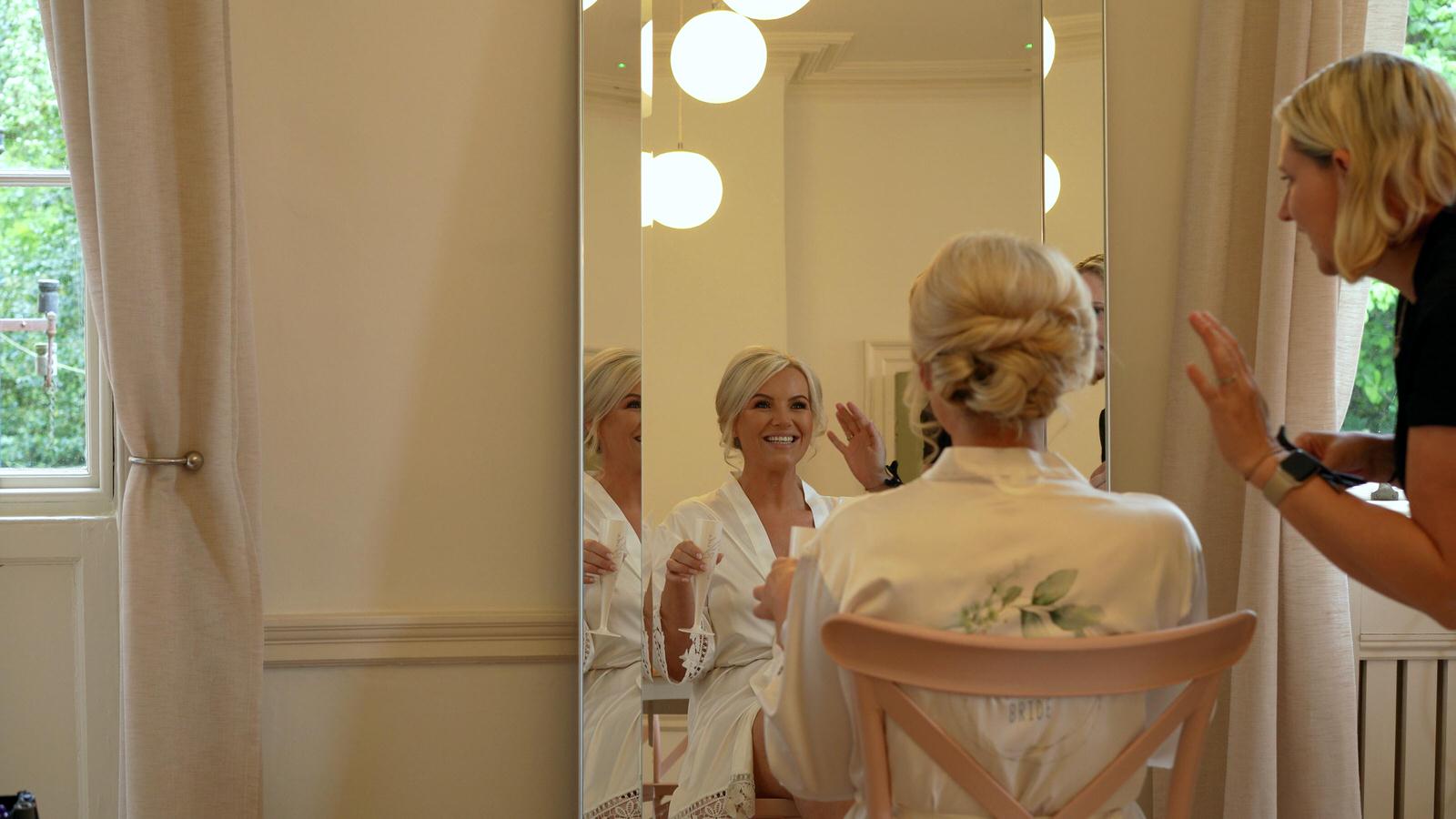 bride smiles at hairdresser in mirror at Rivington hall barn