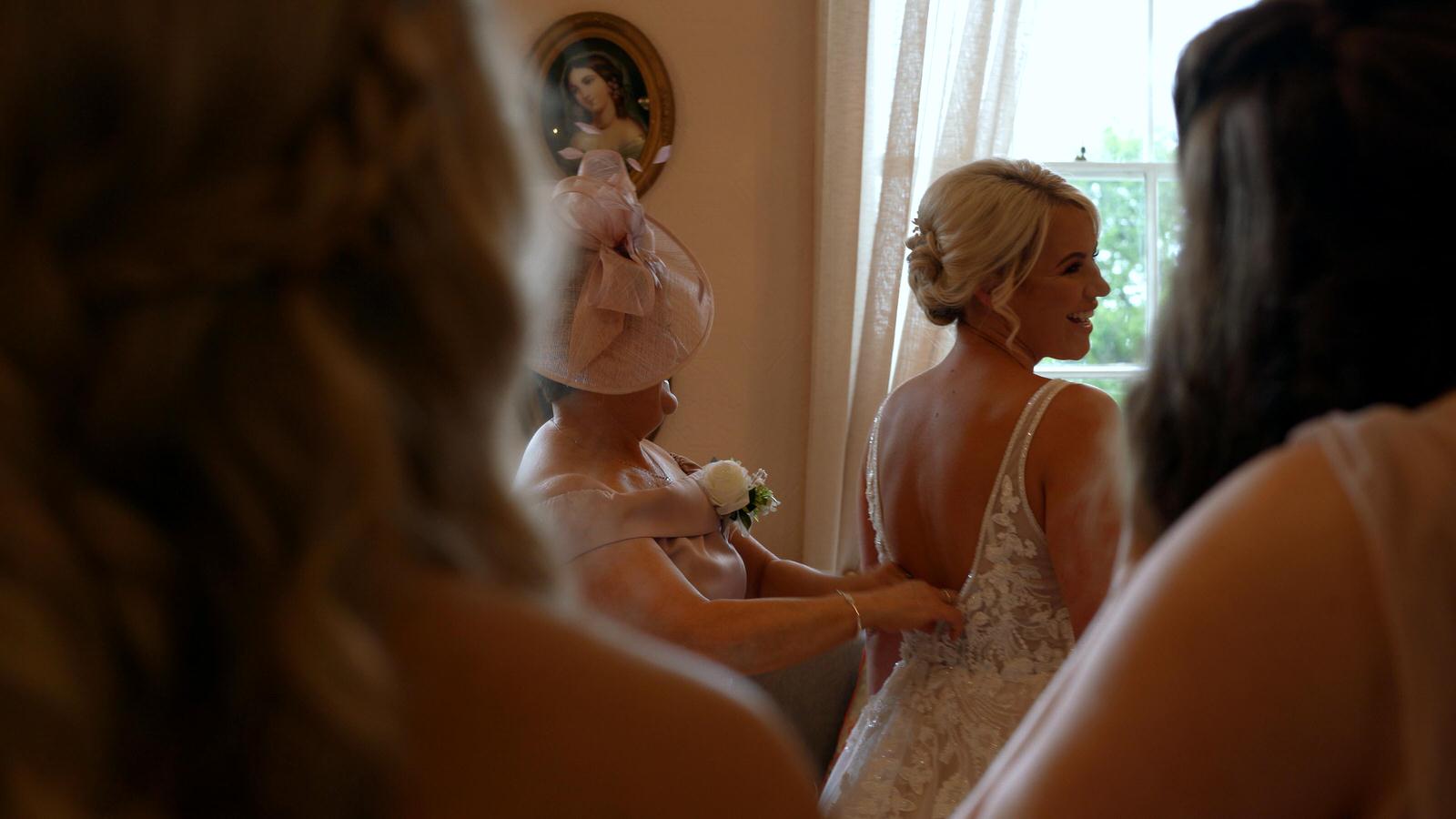 brides mum helps bride in to her wedding dress