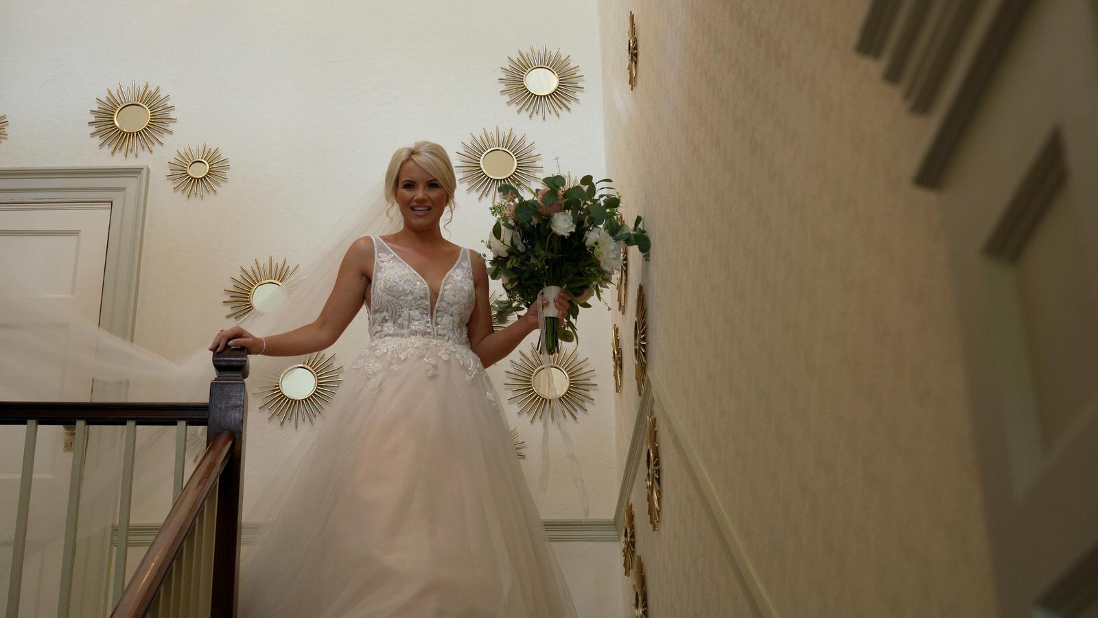 bride walks down the grand stairs at Rivington hall barn