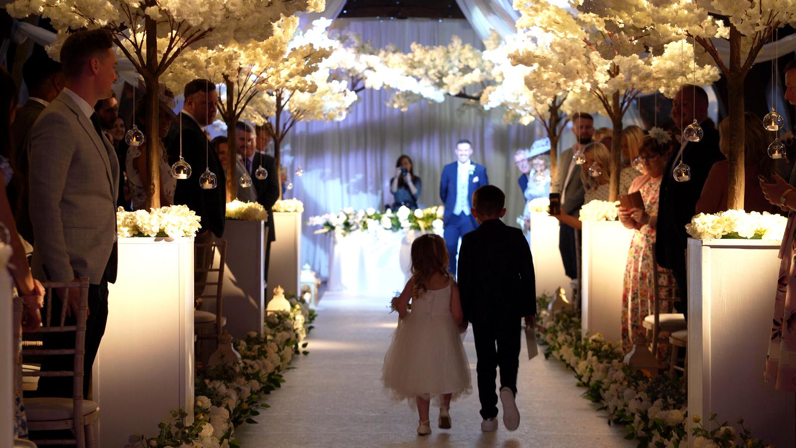 children walk up the aisle towards their dad at Rivington hall barn