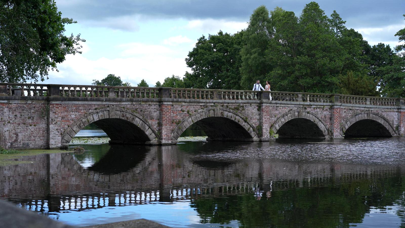 couple walk across bridge at Capesthorne Hall lake