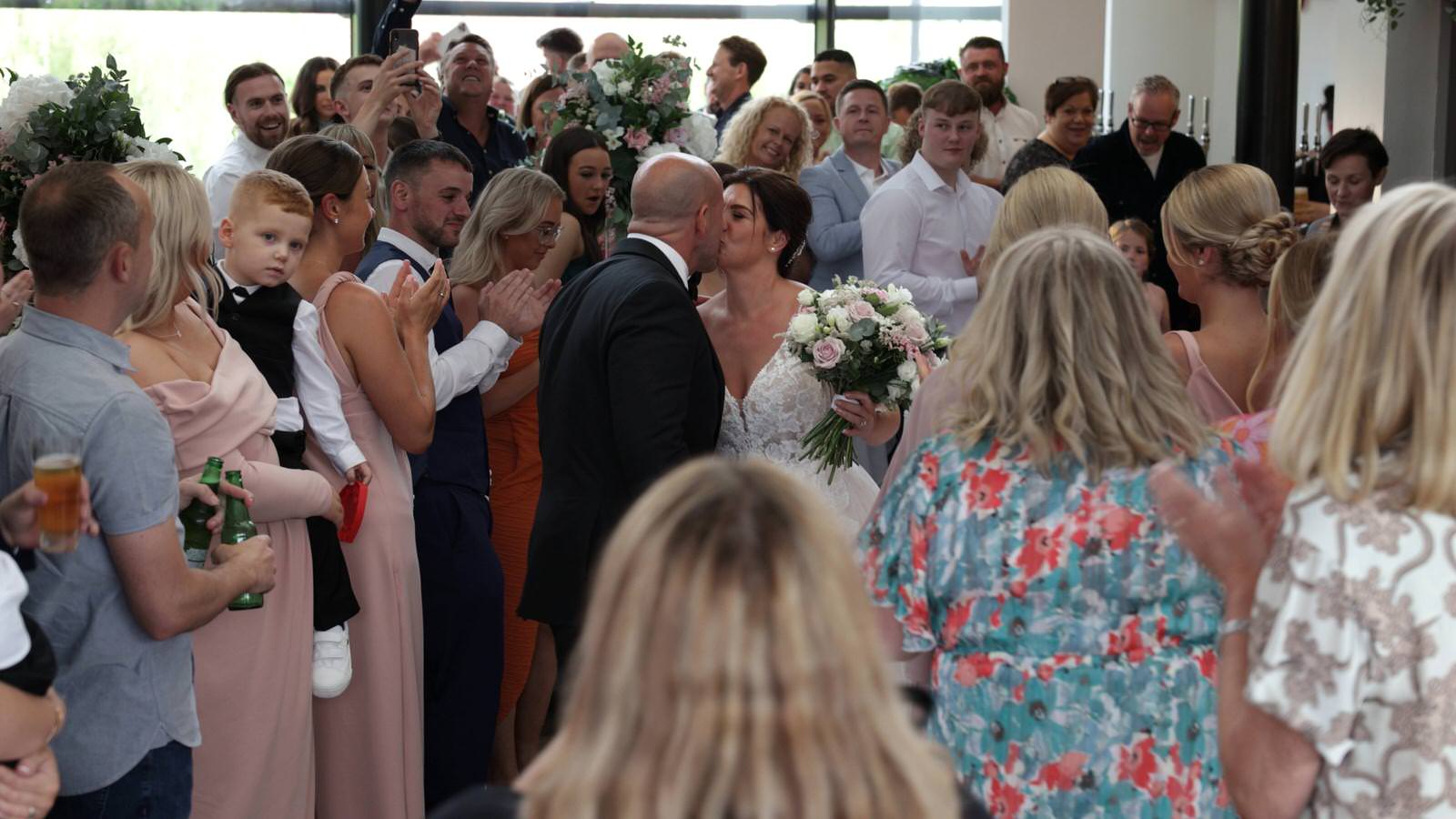bride and groom kiss in a crowded The Castlefield Rooms Manchester