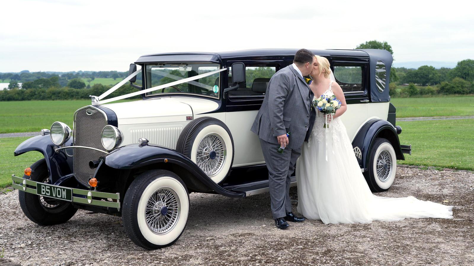 couple pose by wedding car
