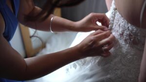 bridemaid fastens buttons on brides dress