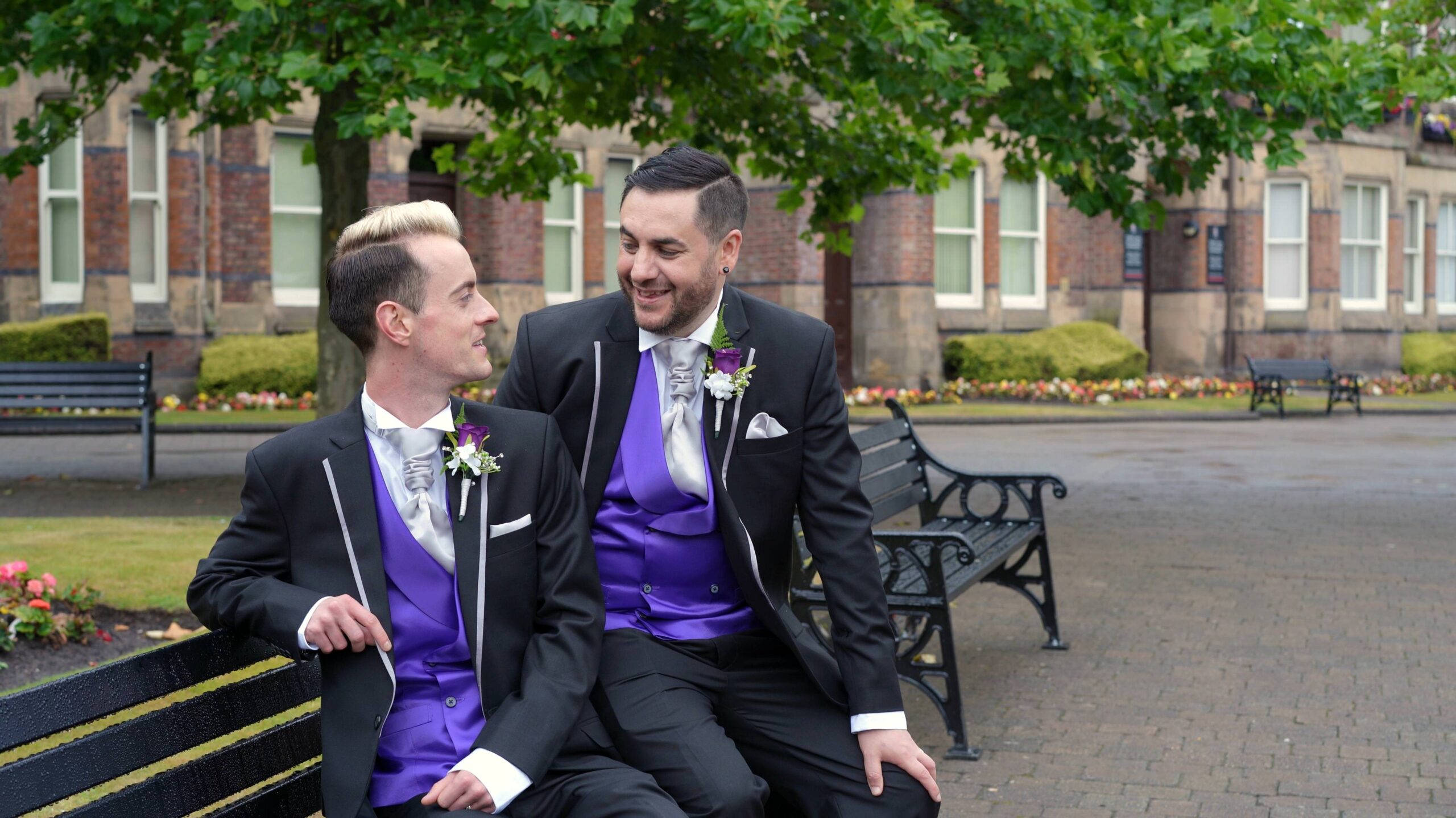 grooms in matching suits sit on park bench