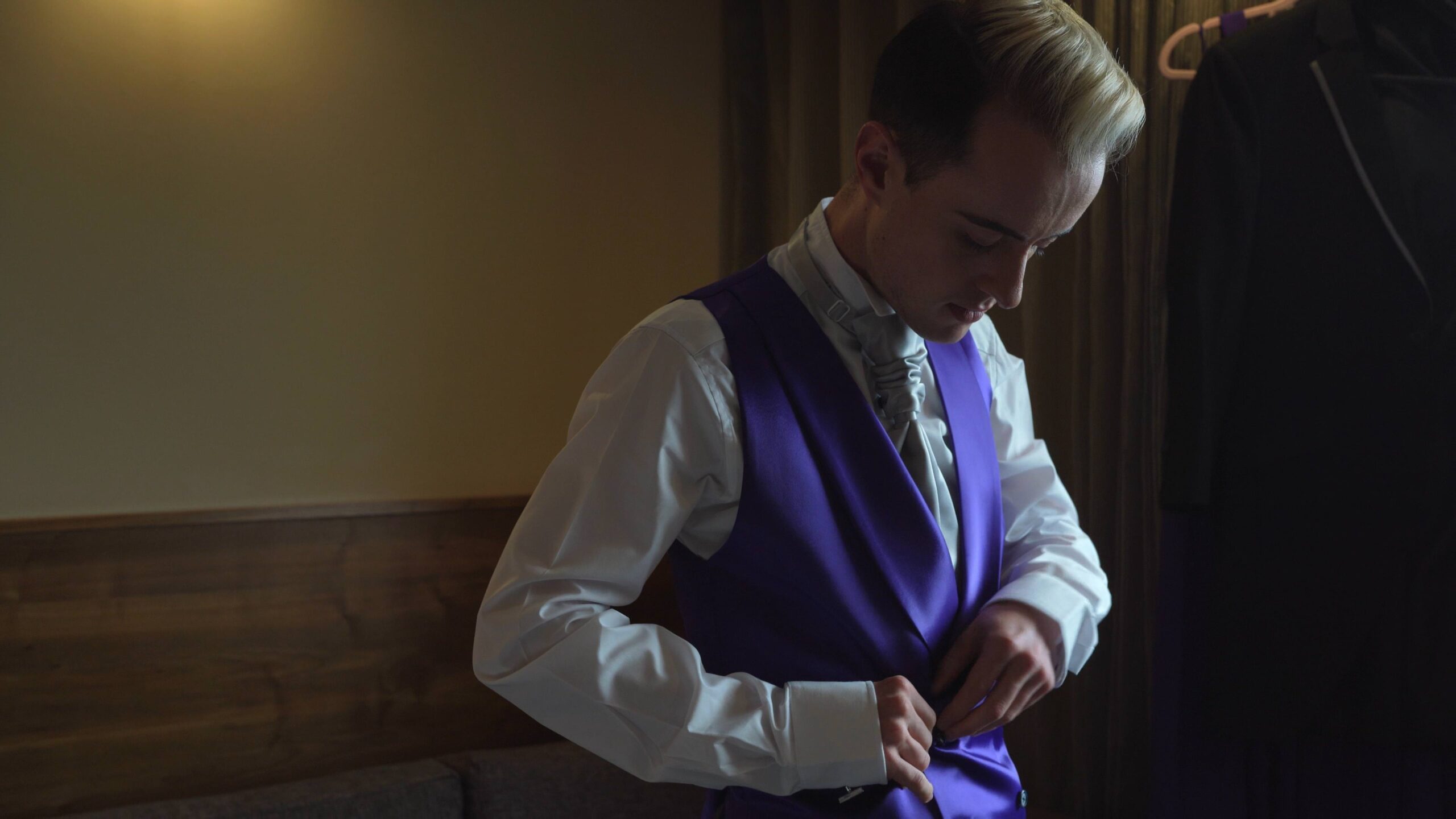 groom fastens buttons on purple satin silk waistcoat