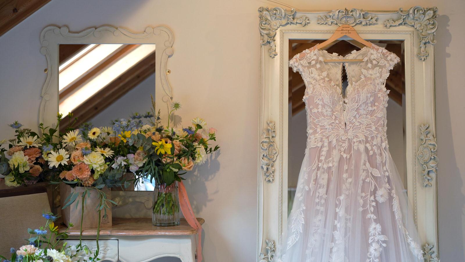 Kerry and Nicks Oaktree Peover wedding 2 wedding dress hanging next to bridal bouquet in cheshire
