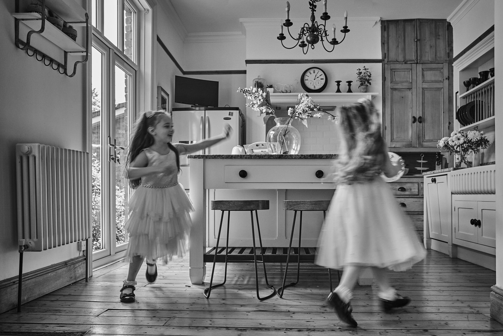 two girls in christening dresses run around their kitchen in Ainsdale