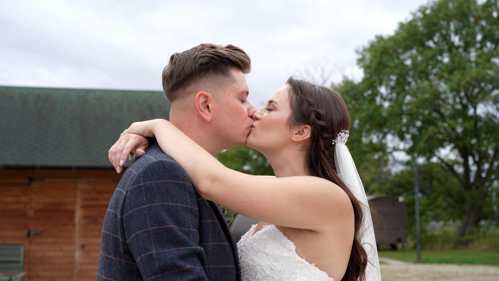 the couple cuddle up and kiss for the videographer and photographer at Charnock Farm