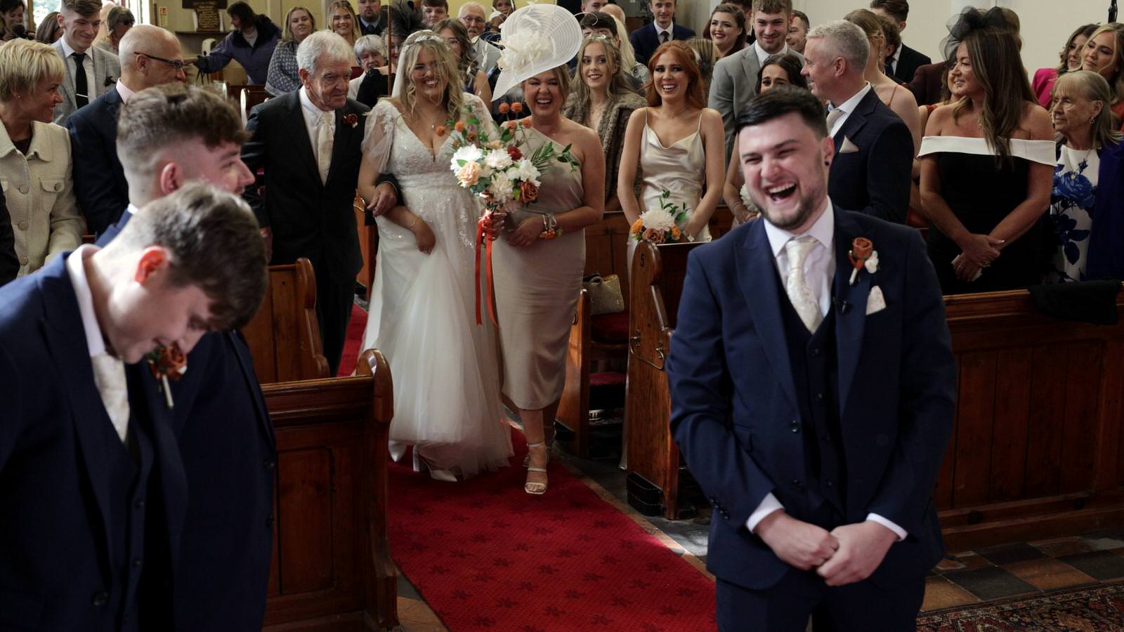 Hannah and Jakes Lancashire Farm Wedding Video 13 groom laughs at bride and grandad walking down the aisle