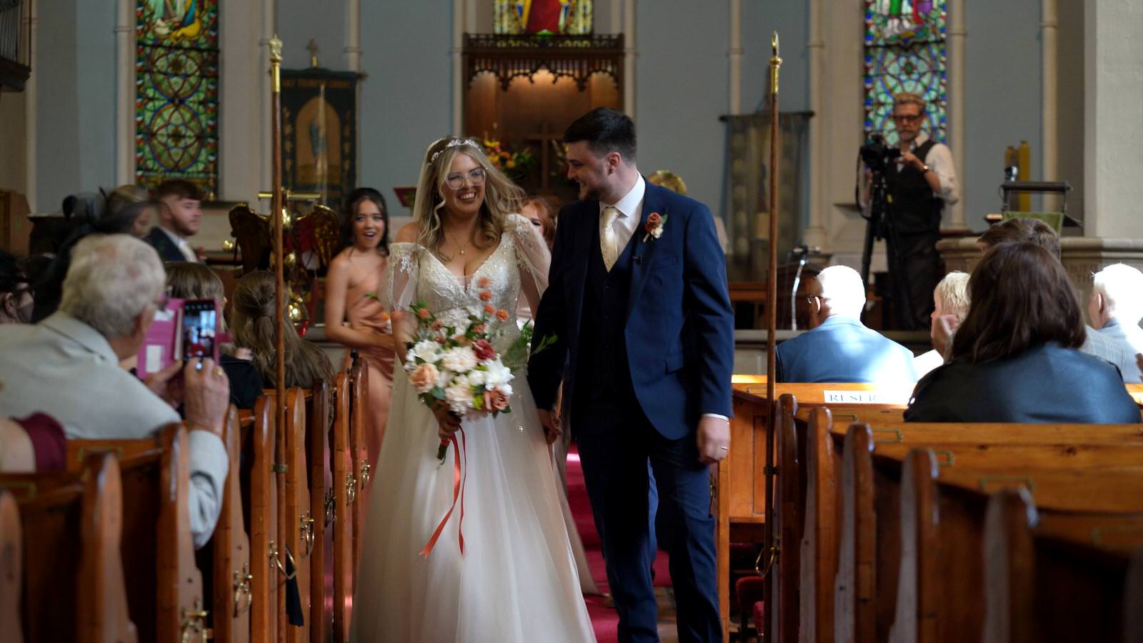 couple smile and walk towards videographer during Holy Trinity Church wedding