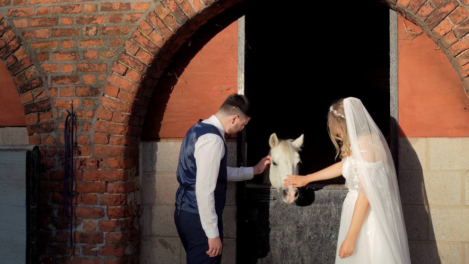 couple stroke a pony during their family farm wedding in lancashire