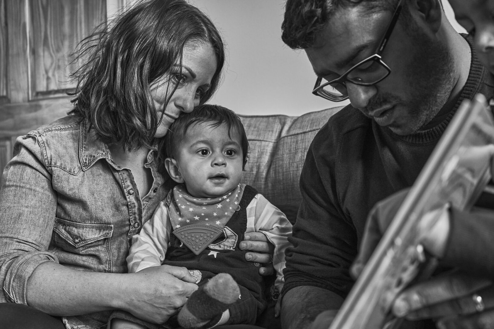a natural documentary style photo of mum cuddling in to her baby whilst dad reads a book