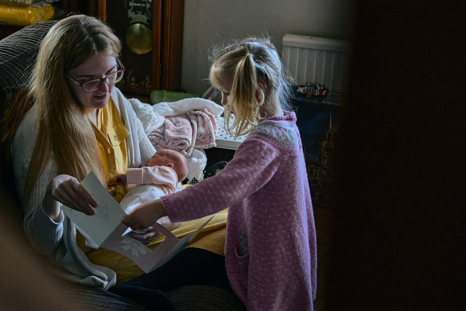 mother holds a sleeping baby and plays with her older child at home