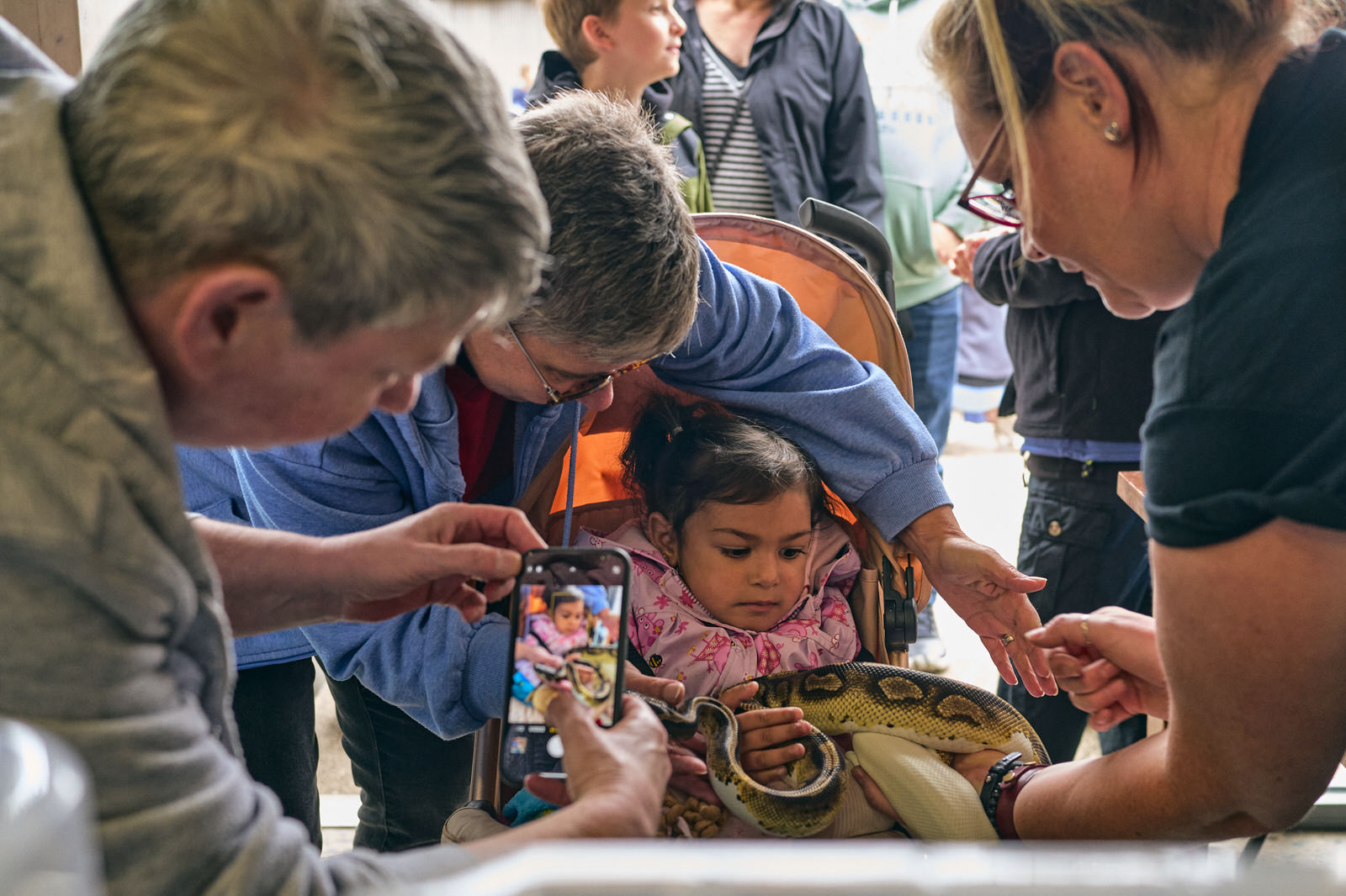 a family huddle around a toddler in a pram holding a snake
