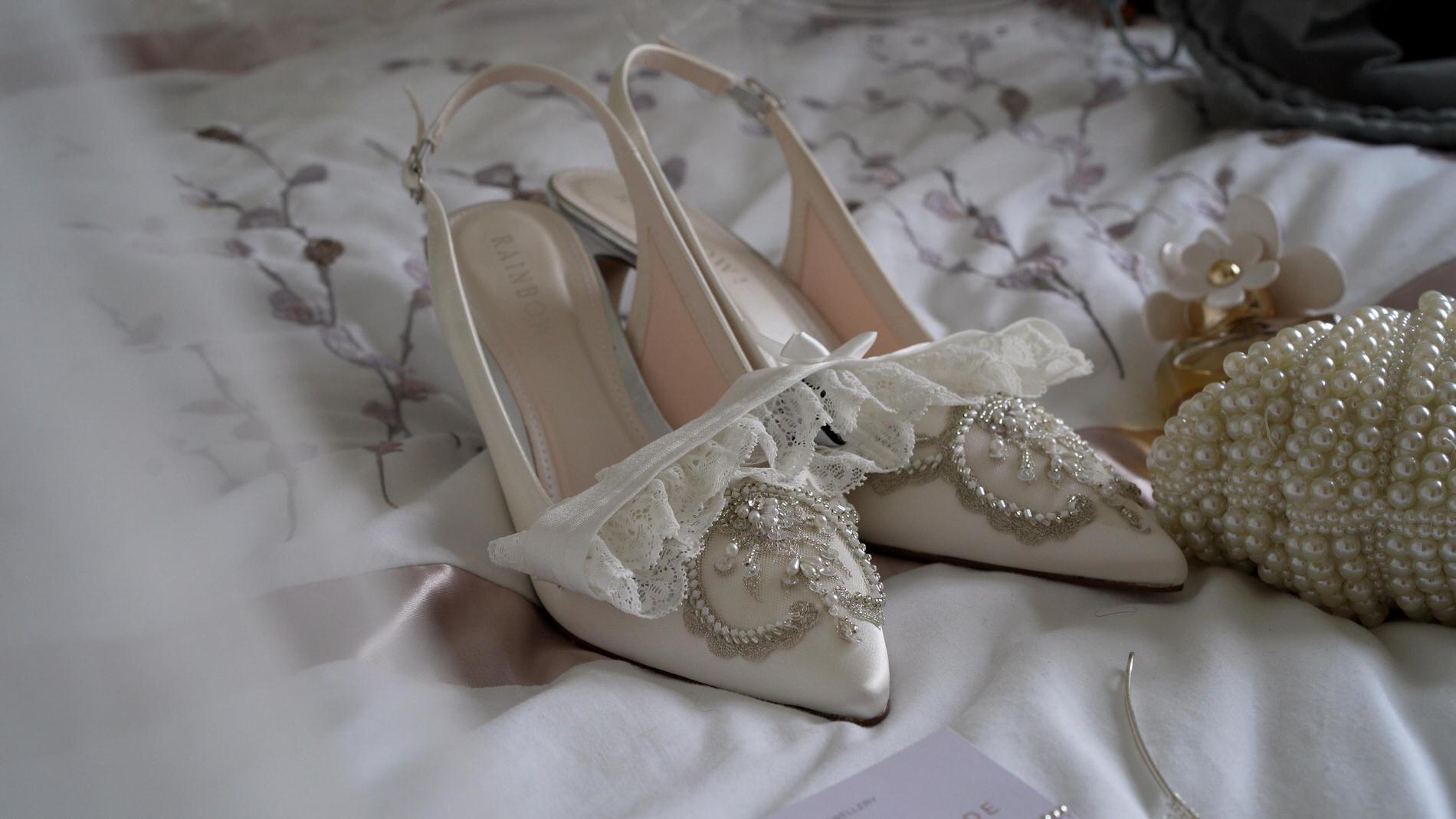 satin wedding shoes sit on a bed with a veil