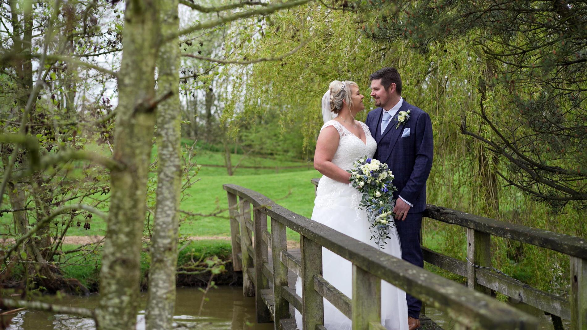a bride and groom stand on the lake bridge at Charnock Farm in Leyland