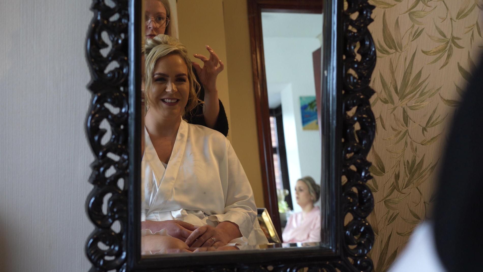 a bride laughs with the hairdresser in the mirro
