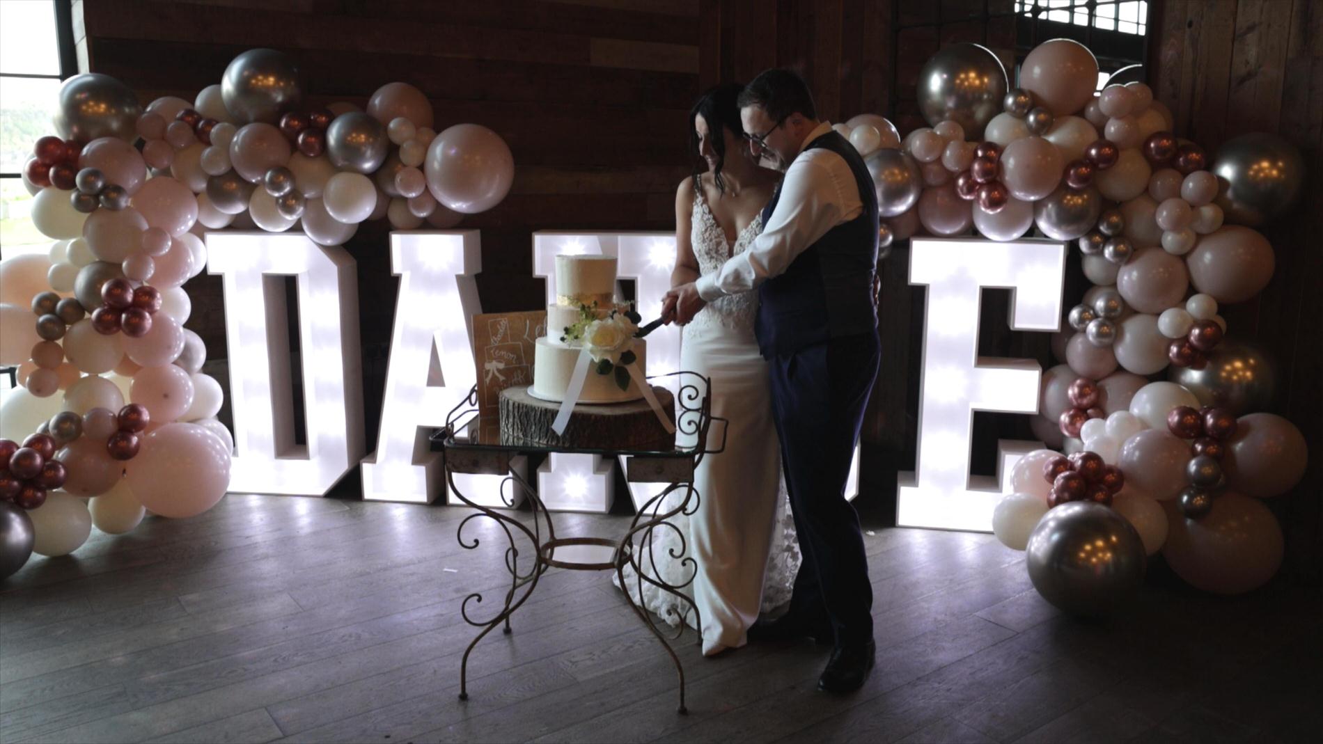 couple cut the cake in front of large light up dance letters