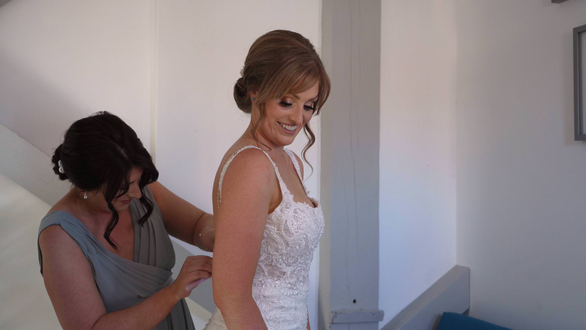 the brides sister helps fasten her dress buttons