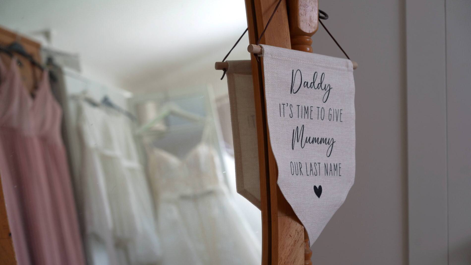 a wedding dress hangs in the reflection with a sign about mummy taking their name