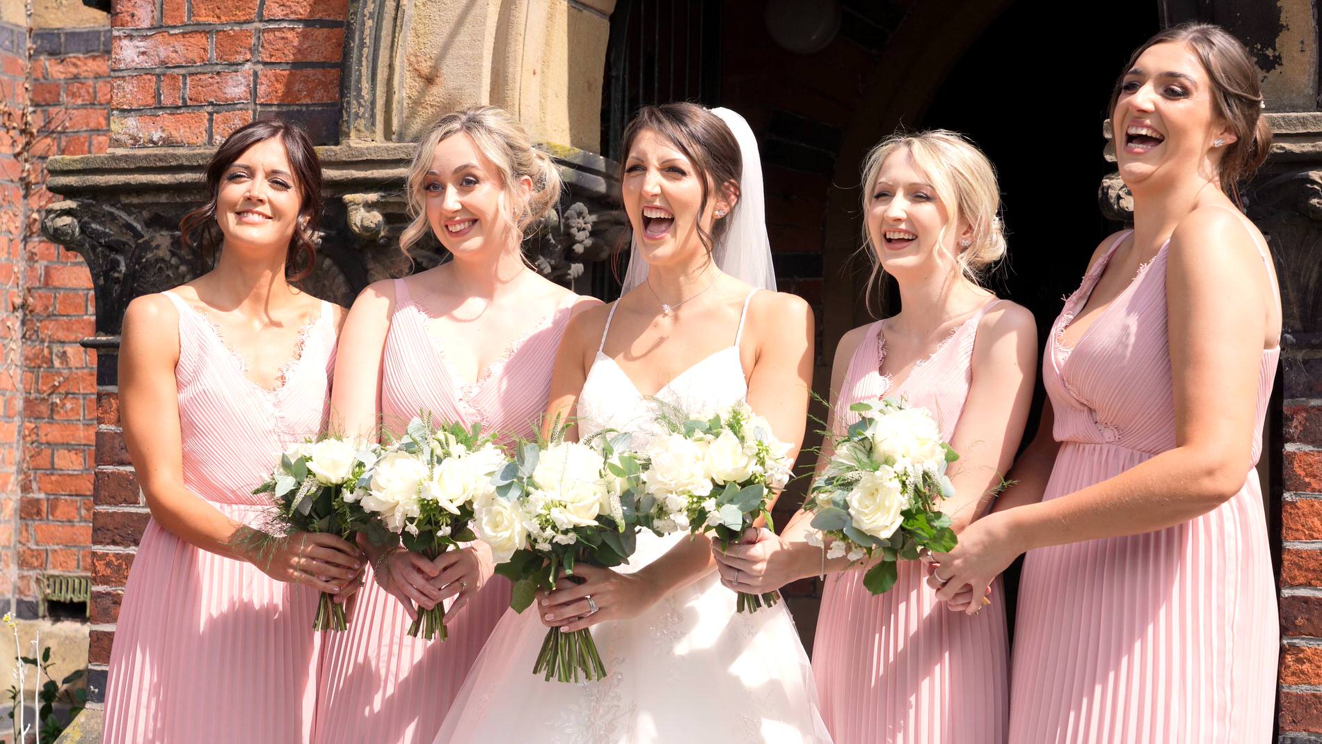 the bride stands with her bridesmaids dressed in blush pink