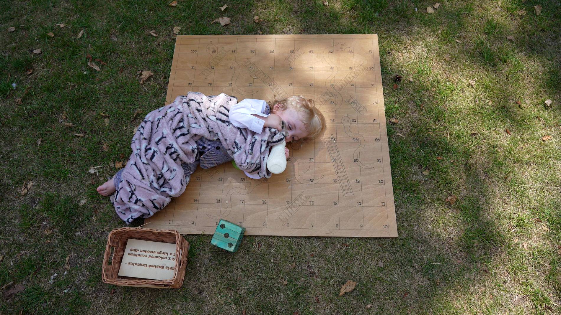 a toddler curls up with his blanket on a garden game