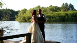 a couple stand in golden hour light by the water at Nunsmere hall