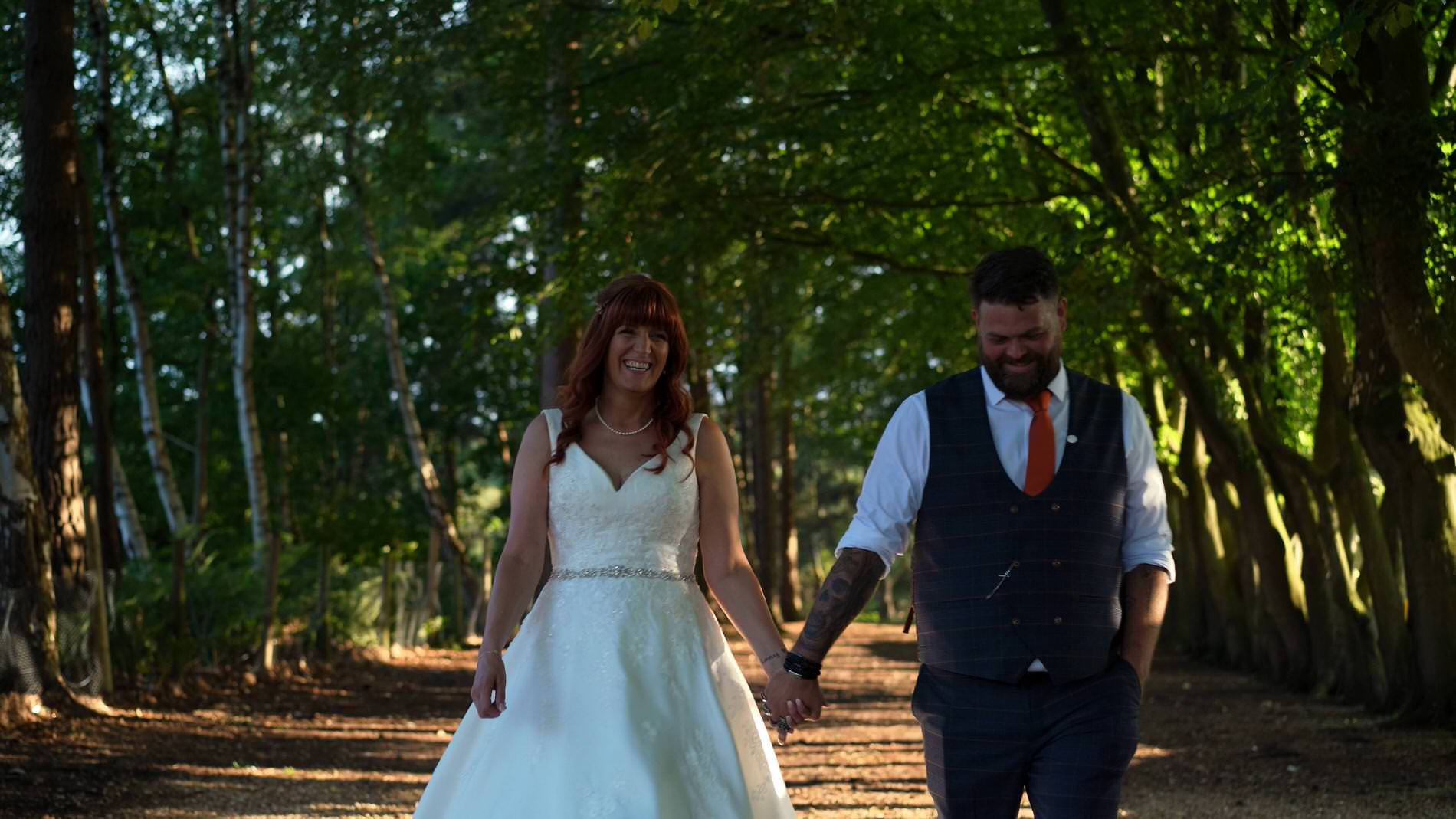 a couple walk by tall trees for the videographer at Nunsmere hall